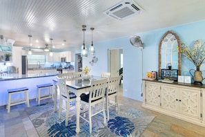 Une cuisine moderne dotée d’un îlot central, de luminaires suspendus et d’un coin repas avec des chaises blanches et un tapis bleu.
