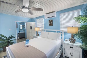 A hotel room with a bed, two bedside tables, a ceiling fan, an air conditioning unit, and a potted plant. - Private Pool | 3 Mins to Welches Beach | BBQ (Oistins)