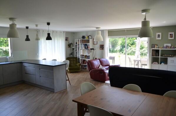A modern kitchen with a central island, a dining area with a wooden table, and a red leather sofa.