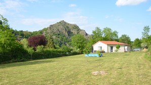 A house with a red roof, surrounded by a grassy field and trees, with a mountain in the background. - Charming country house (Chamalières-sur-Loire)