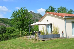 A modern house with a red-tiled roof, a patio area with a table and chairs, and a view of a mountain in the background.