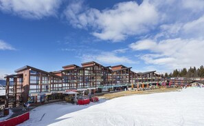 Um moderno edifício de estação de esqui com vários níveis e varandas, rodeado por neve.