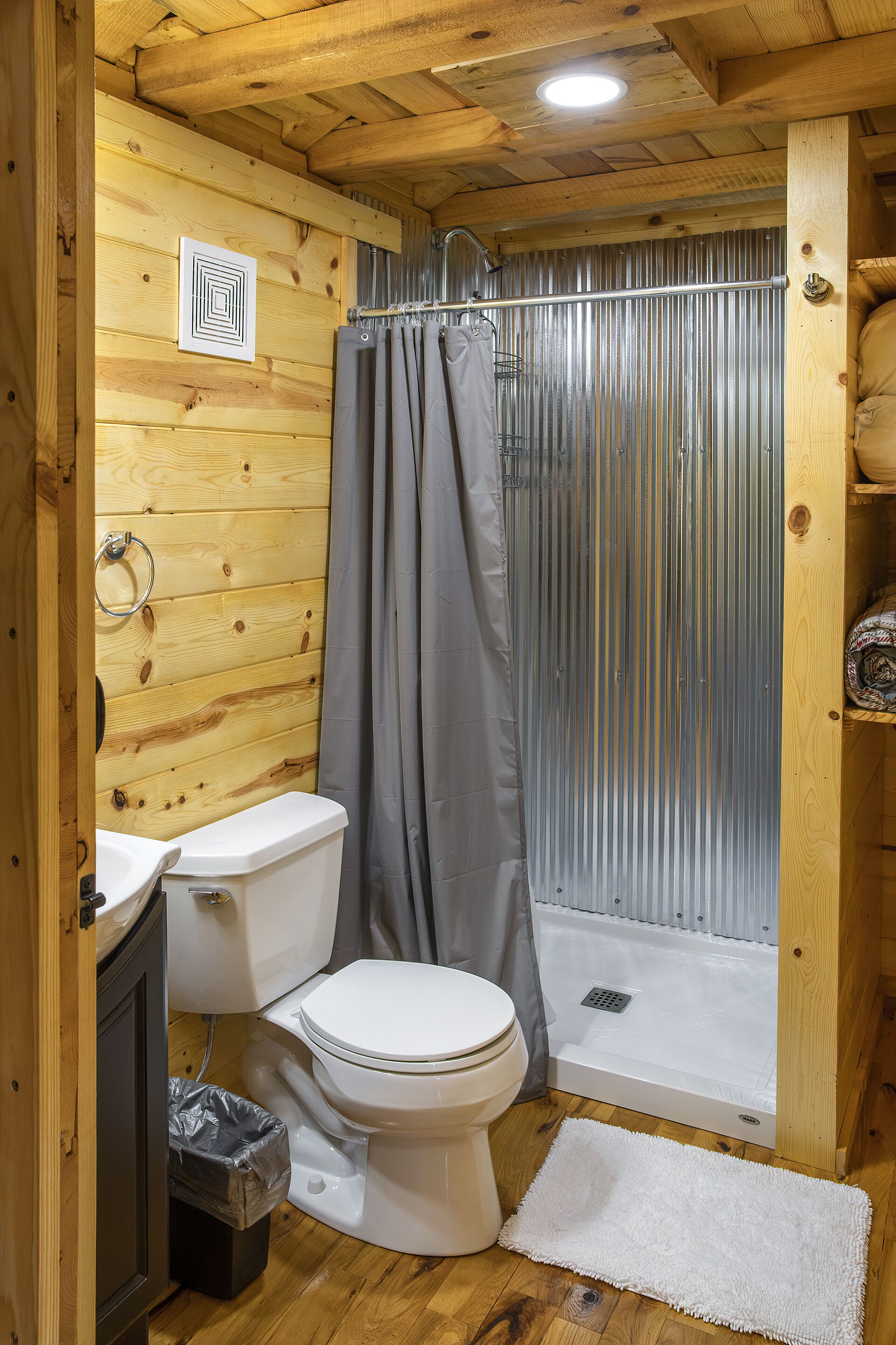 A wooden cabin bathroom with a toilet, shower, and a small sink.