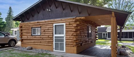 A log cabin with a covered porch, a door with a window, and a small window on the side.