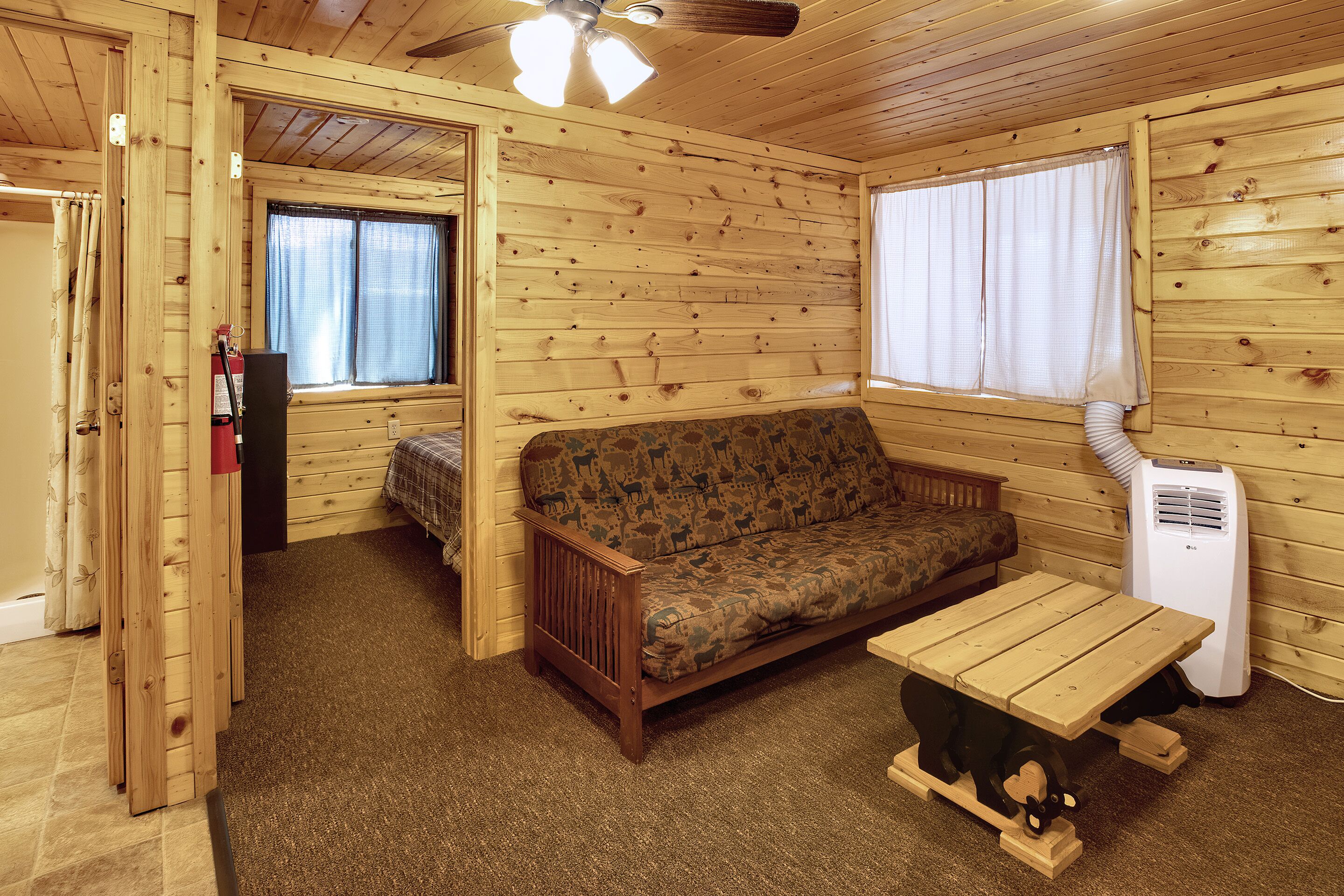 A cozy cabin interior with a wooden floor, a sofa, a table, and a ceiling fan.