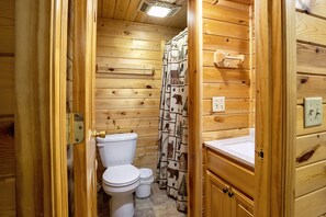 A wooden cabin bathroom with a toilet, a shower curtain with animal prints, and wooden cabinets.