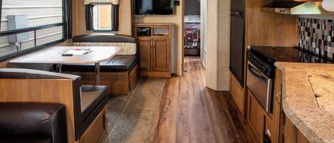 A compact RV interior with a kitchenette, a dining area, and a sleeping space.