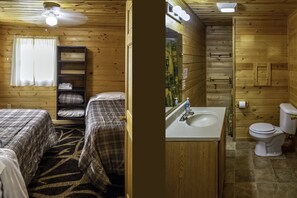 A wooden cabin with two beds, a bathroom, and a ceiling fan.