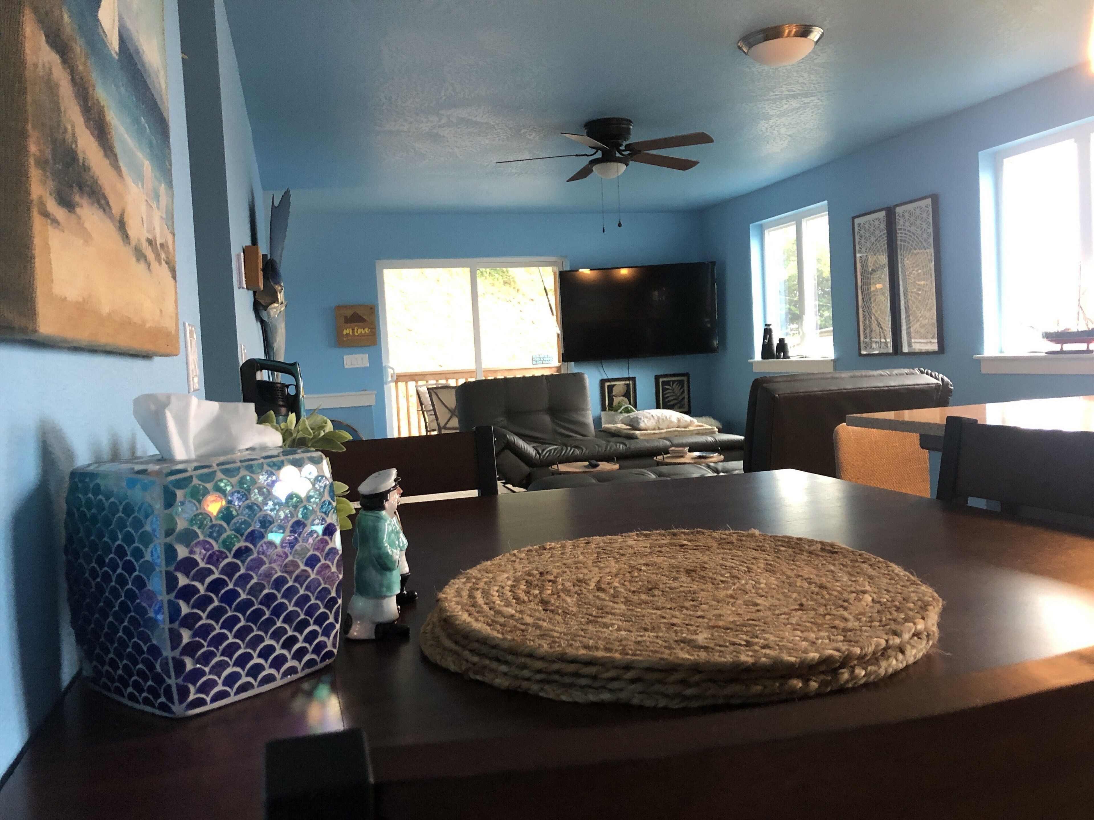 Ein Wohnzimmer mit blauer Wand, Deckenventilator, Flachbildfernseher, Couchtisch und Esstisch.