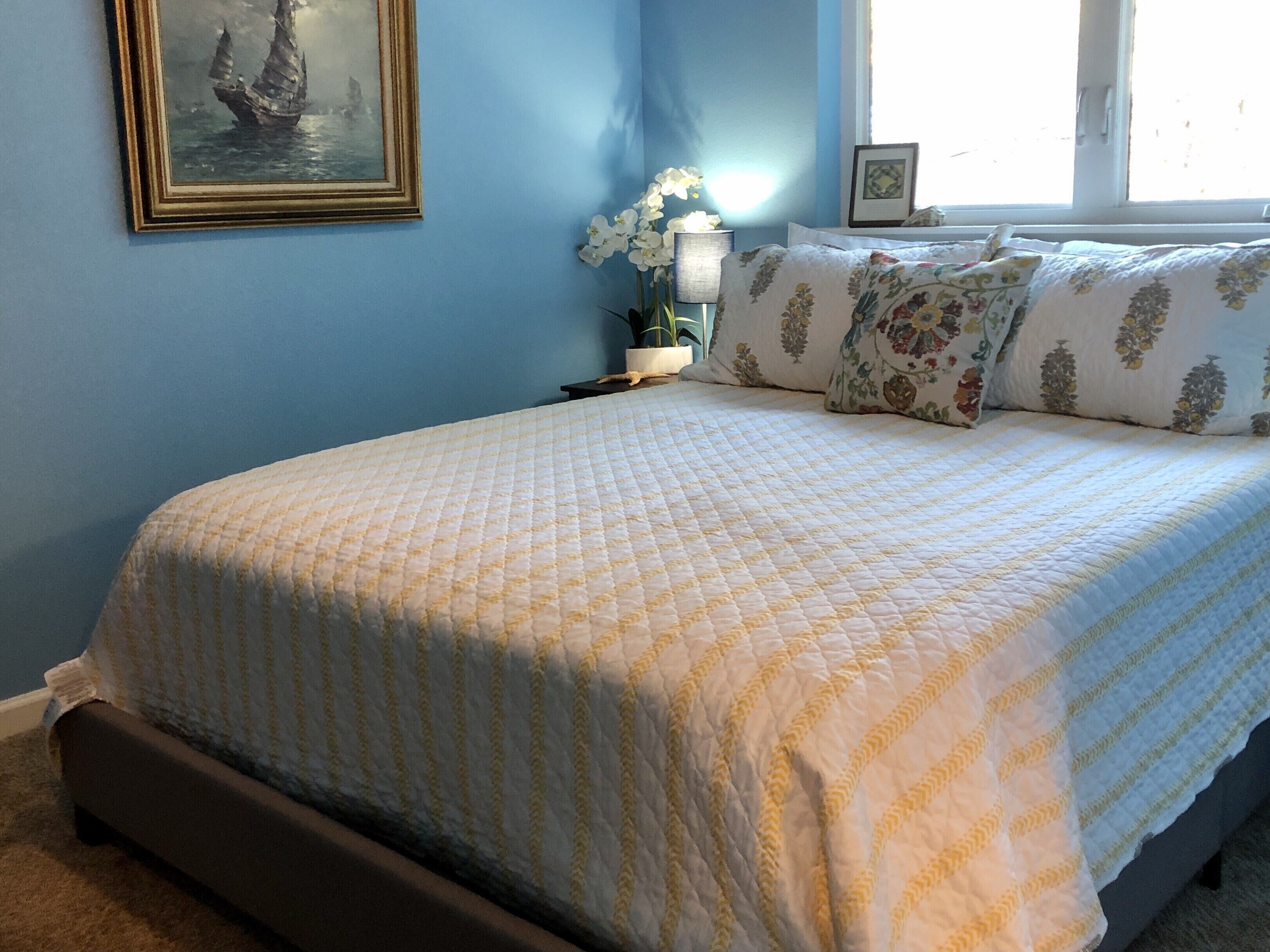 A bedroom with a bed, a nightstand, a lamp, a framed picture, and a window.