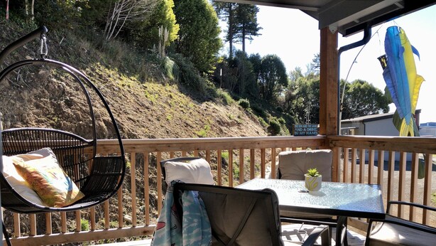 Un área de estar al aire libre techada con mesa y sillas, un sillón colgante y vistas a una ladera.