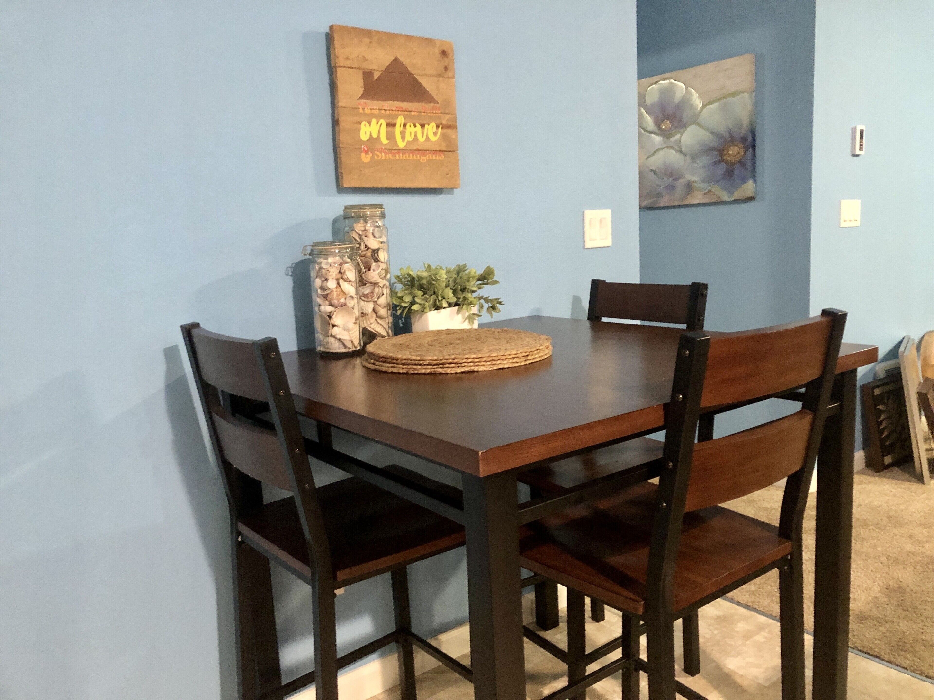 A dining table with four chairs, a jar of nuts, a small plant, and a placemat.