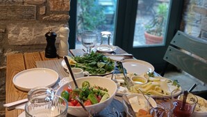 A table set with various dishes, including salads, cheeses, and fruits, in a room with stone walls and a view through a glass door. - Pulinda Pansiyon (Soke)