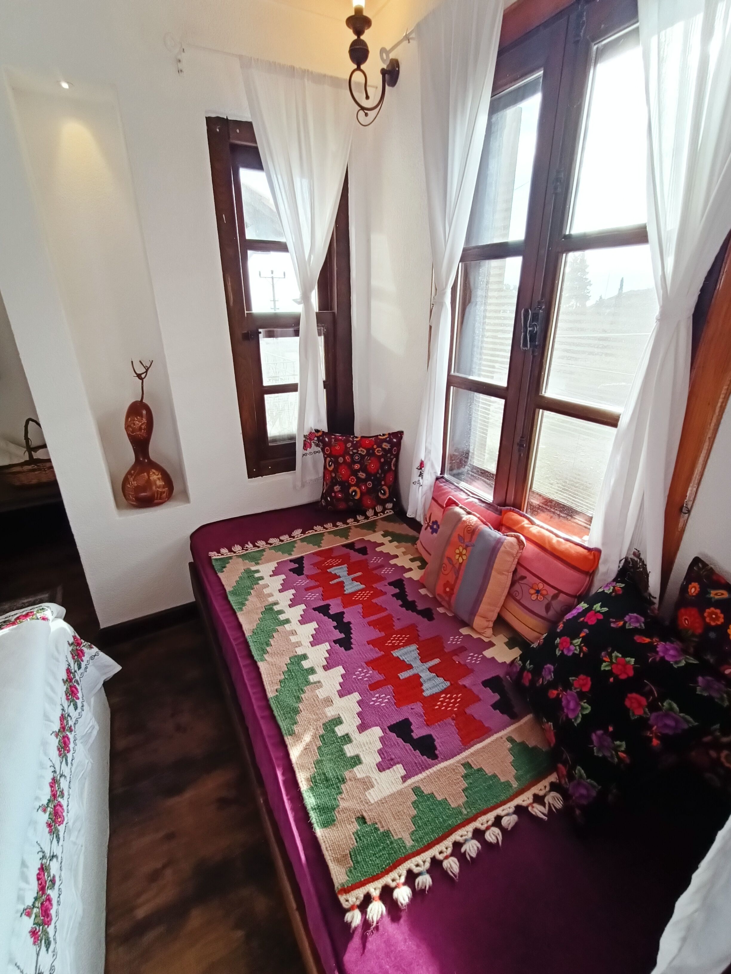 Een gezellige slaapkamer met een groot bed, een raam met gordijnen en een decoratieve vaas op het nachtkastje.