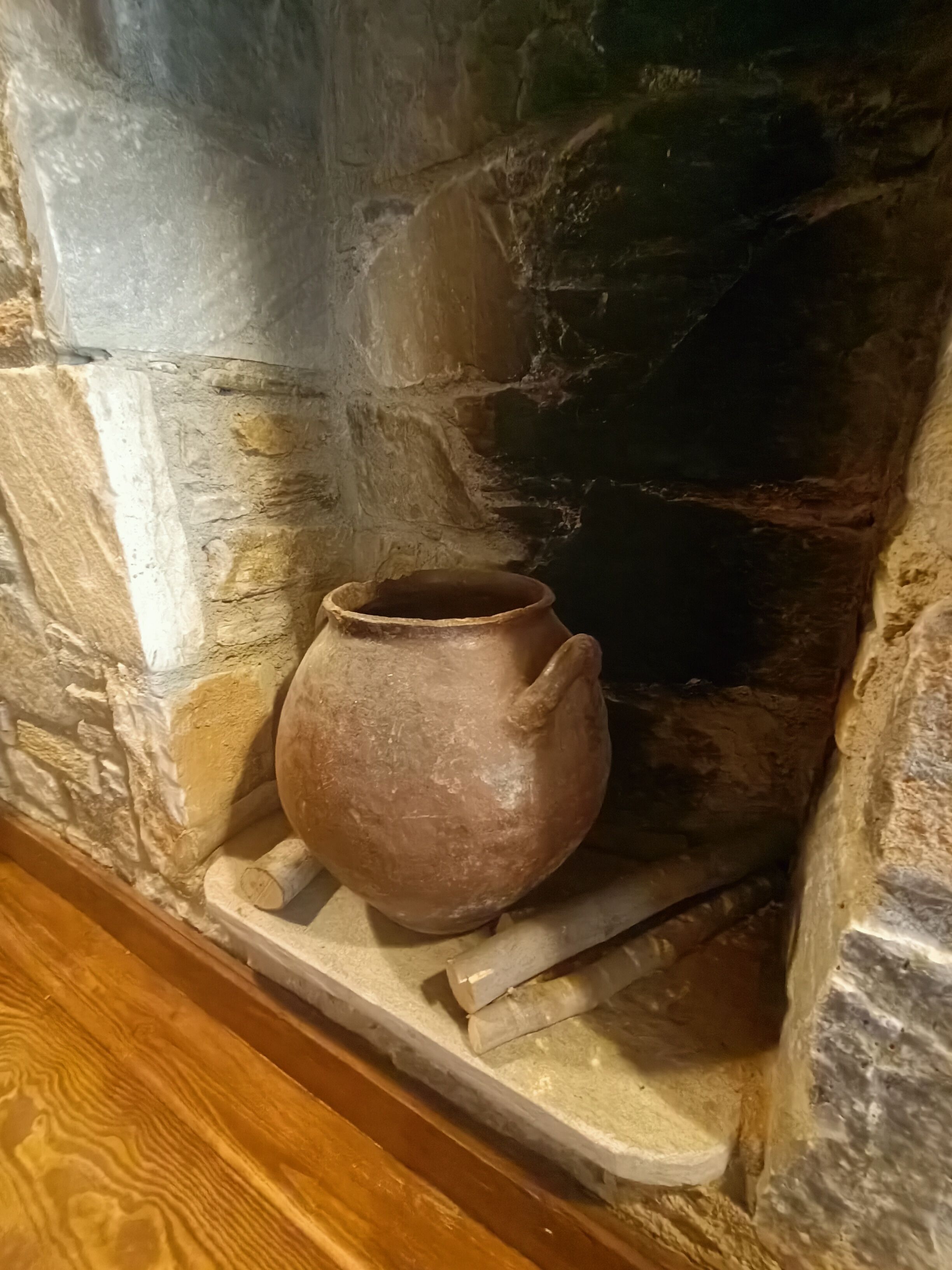 A stone fireplace with a rustic clay pot placed on a shelf.
