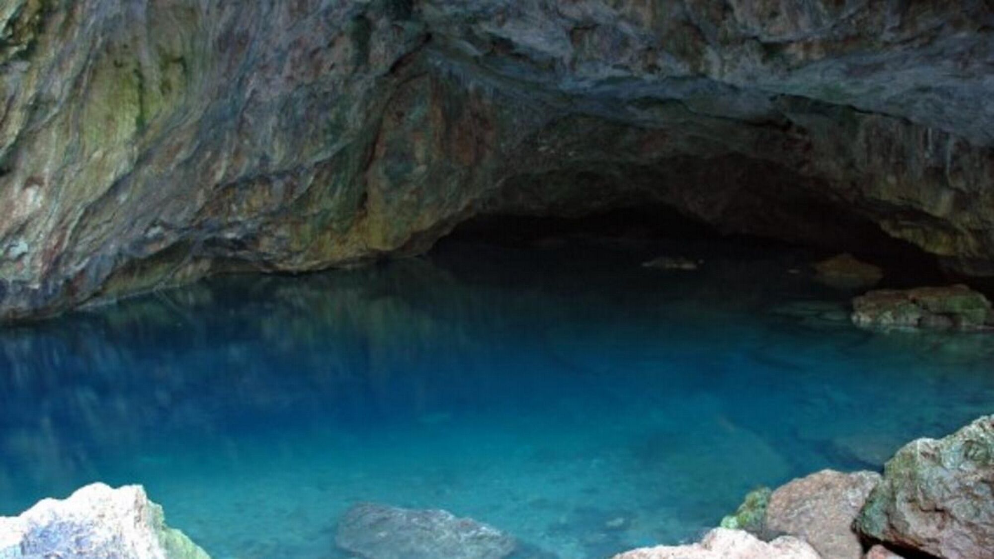 A cave entrance with clear blue water and rocky formations.