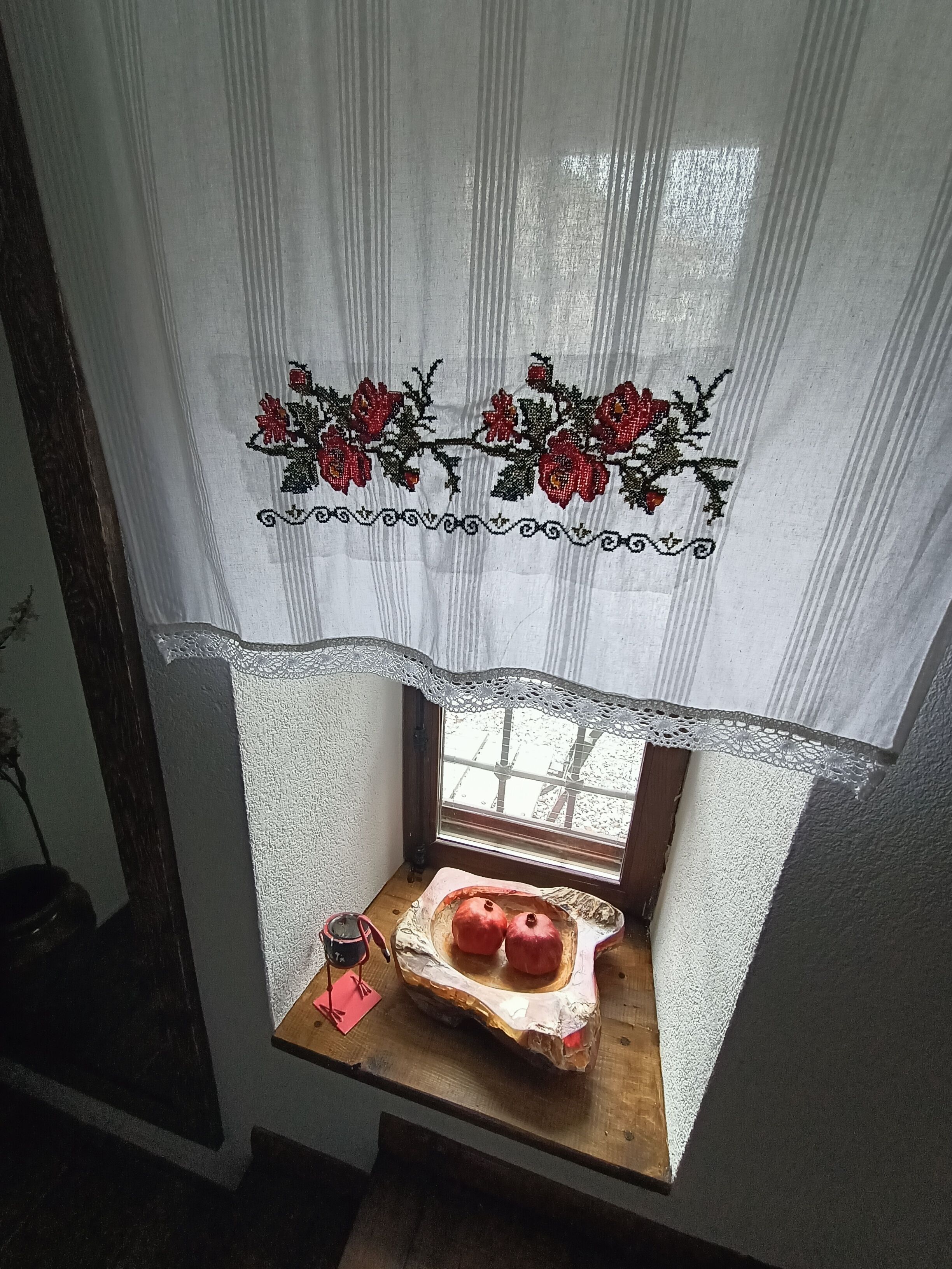 Una ventana con cortina de encaje y una pequeña estantería de madera debajo.