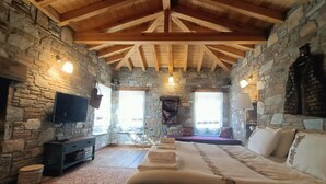 A stone-walled room with a wooden ceiling, a bed, a TV, and a fireplace. - Pulinda Pansiyon (Soke)