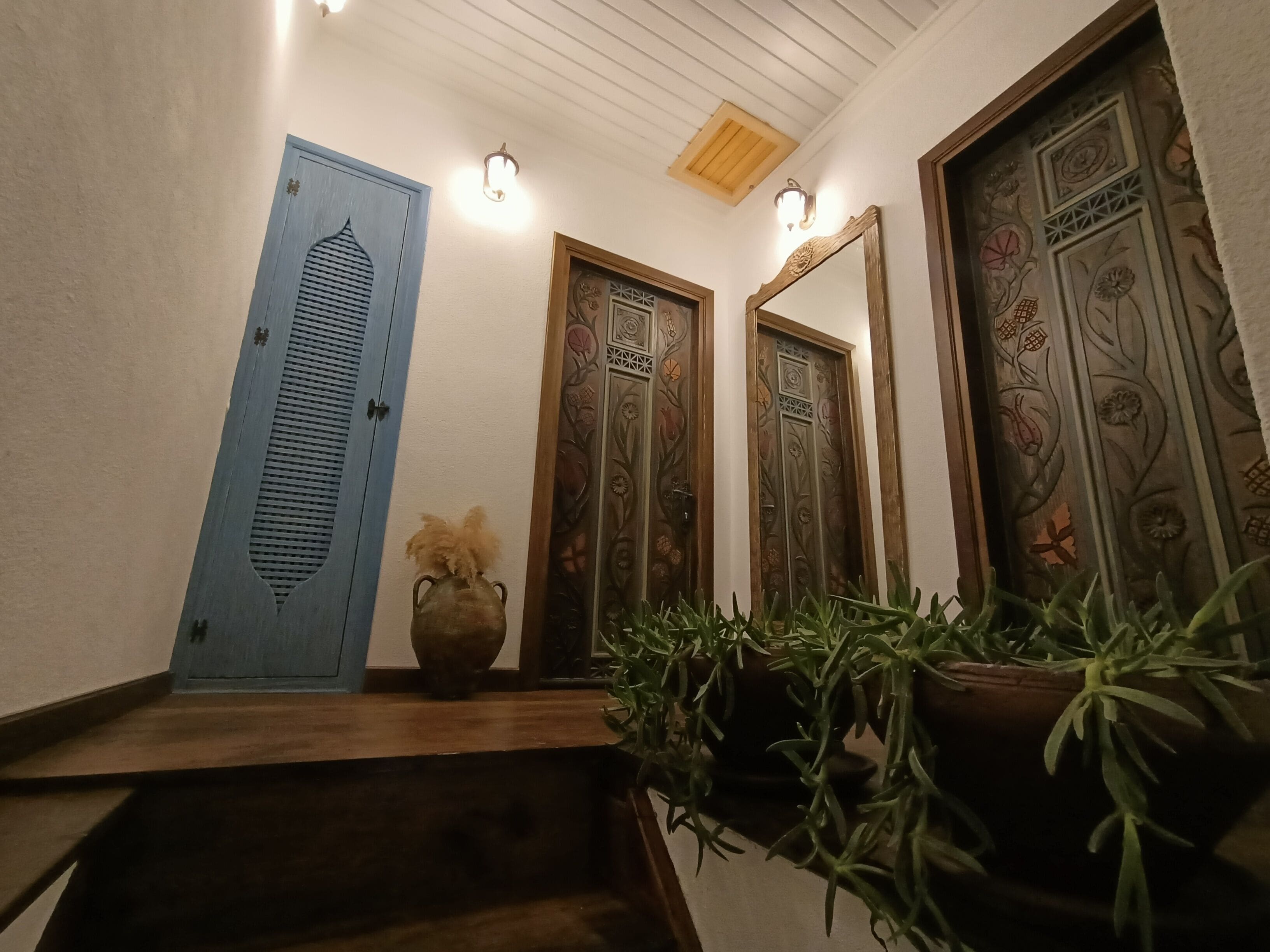 A hallway with a blue door, a decorative mirror, and potted plants.
