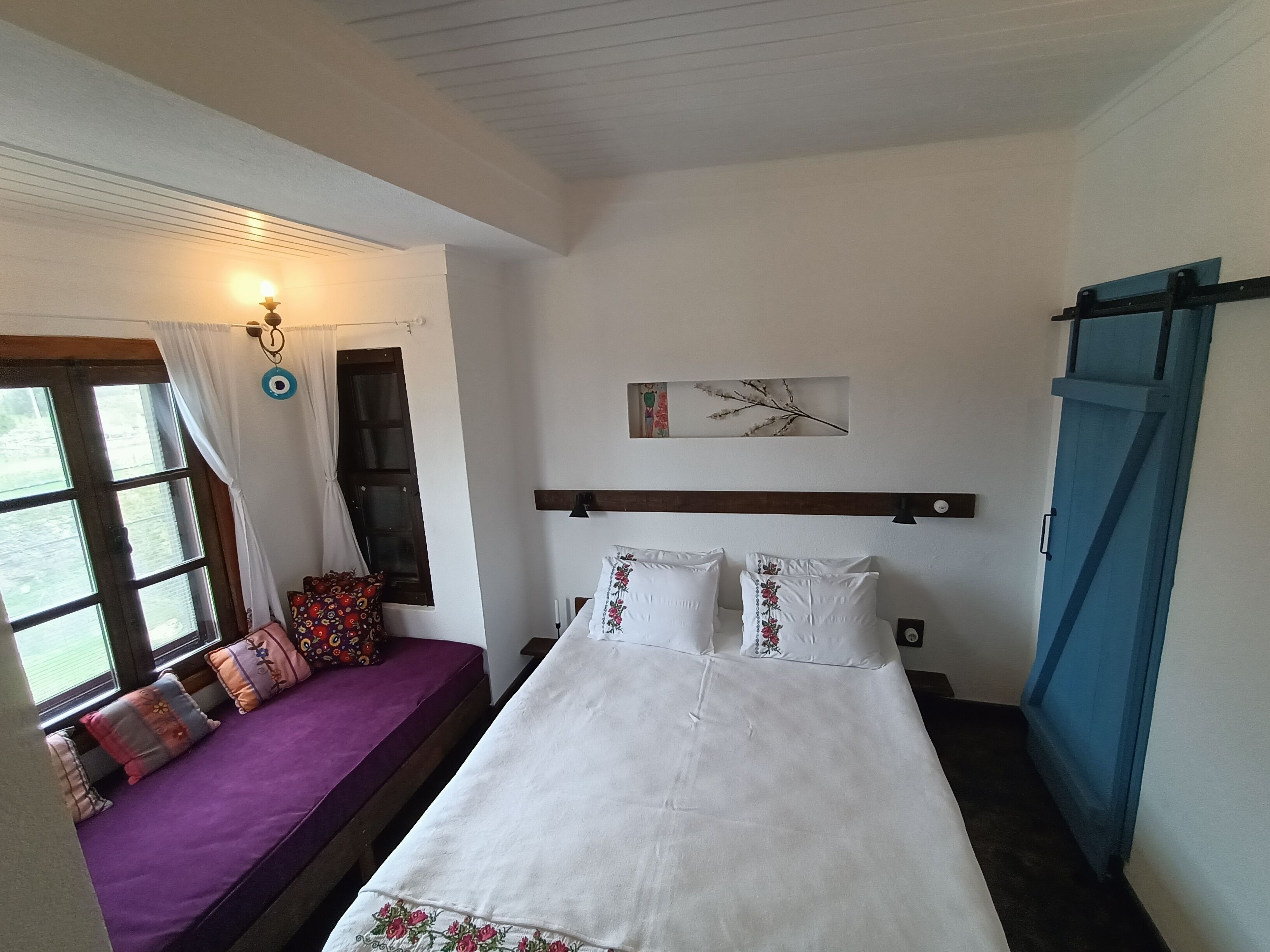 Un dormitorio con cama, una ventana con cortinas, una mesita de noche y una obra de arte colgada en la pared.
