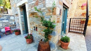 A stone building with a small outdoor seating area, potted plants, and a metal gate. - Pulinda Pansiyon (Soke)