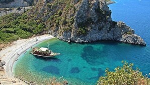 A boat anchored near a rocky coastline with clear turquoise waters. - Pulinda Pansiyon (Soke)