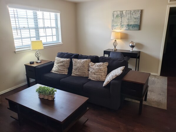 A living room with a dark-colored sofa, two side tables, a lamp, and a small plant on a wooden coffee table. - Economy near Baptist Hospital, 2 Bedroom Condo #202 (Oklahoma City)
