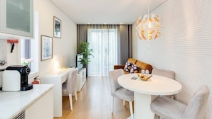 Ein modernes, helles Wohnzimmer mit einem runden Esstisch, einer Couch und einer Kaffeemaschine.