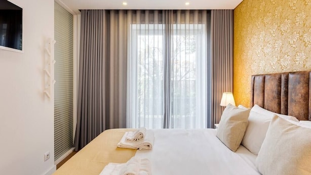 Ein Hotelzimmer mit einem großen Bett, einem Kopfteil, einem Fenster mit Vorhängen und einer Wand mit floralem Muster.
