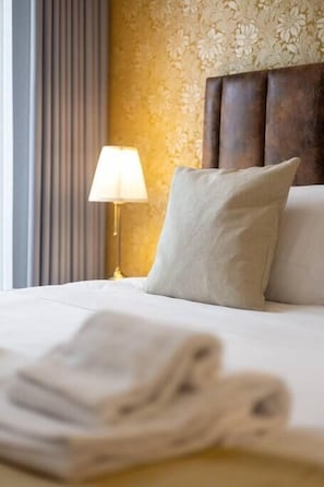 Un lit bien fait, avec un oreiller et une serviette pliée, une lampe de chevet et un mur décoré d’un motif.