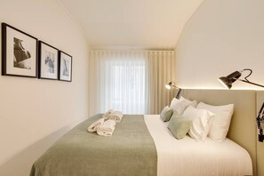 A neatly made bed with a green blanket, a set of towels, and a bedside lamp.