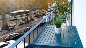 A balcony with a blue table and potted plants, overlooking a street with parked cars and a tram. - *NEW* Riverside 2 Bedroom Apartment by DA'HOME (Porto)