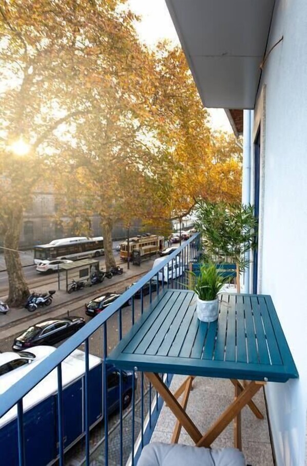 A balcony with a blue table and potted plants, overlooking a street with parked cars and a tram. - *NEW* Riverside 2 Bedroom Apartment by DA'HOME (Porto)