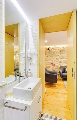 Un baño moderno con un espejo grande, lavamanos blanco y suelo de madera.