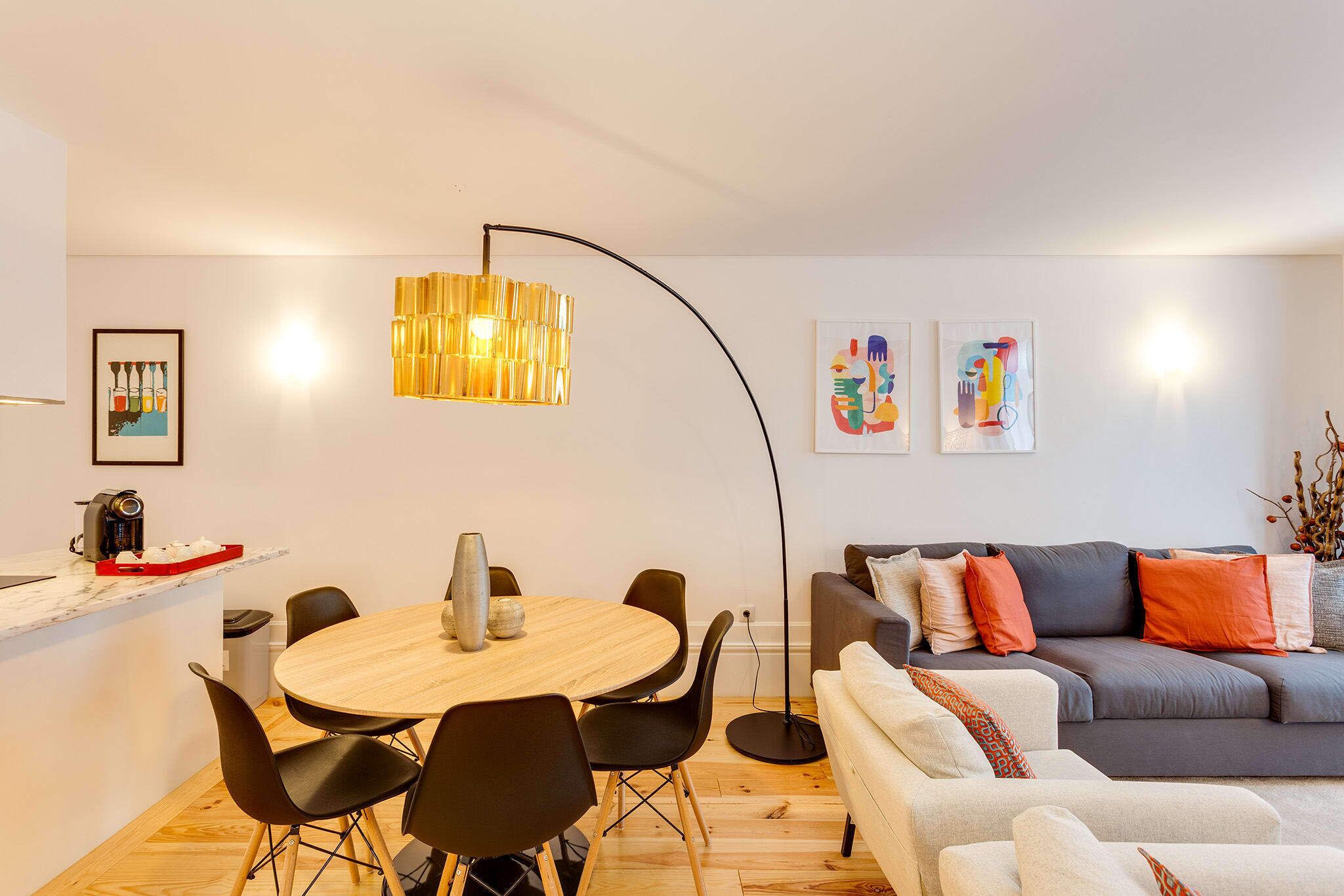 A modern living room with a round wooden table, black chairs, a grey sofa, and a floor lamp.
