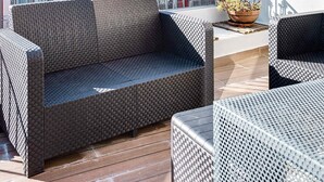 Een balkon met rieten meubilair, een rood gebouw met balkons, en een heldere lucht.