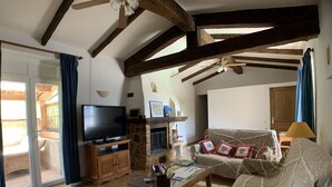 A living room with a stone fireplace, wooden beams, a television, and a sofa. - Gite in Maison d'hôtes in Pays de Fayence - 3 bedrooms Swimming pool, Jacuzzi (Tourrettes)