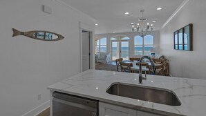 A kitchen with a marble countertop, a fish-shaped mirror, and a view of the ocean through large windows. - Modern Gulf-Front, Sleeps 10, Beach Setup, Pool + Free Attraction Tickets! (Panama City Beach)