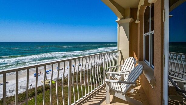 A balcony with white chairs overlooking a beach with people and umbrellas. - Modern Gulf-Front, Sleeps 10, Beach Setup, Pool + Free Attraction Tickets! (Panama City Beach)