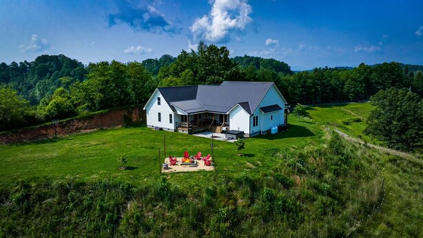 A white house with a covered porch and a fire pit in the front yard.