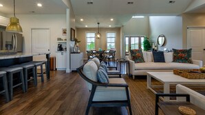 A spacious living area with a sofa, chairs, and a dining table. There is a kitchen area with a refrigerator and a coffee machine.