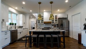 A modern kitchen with white cabinetry, a large island with bar stools, stainless steel appliances, and pendant lighting.