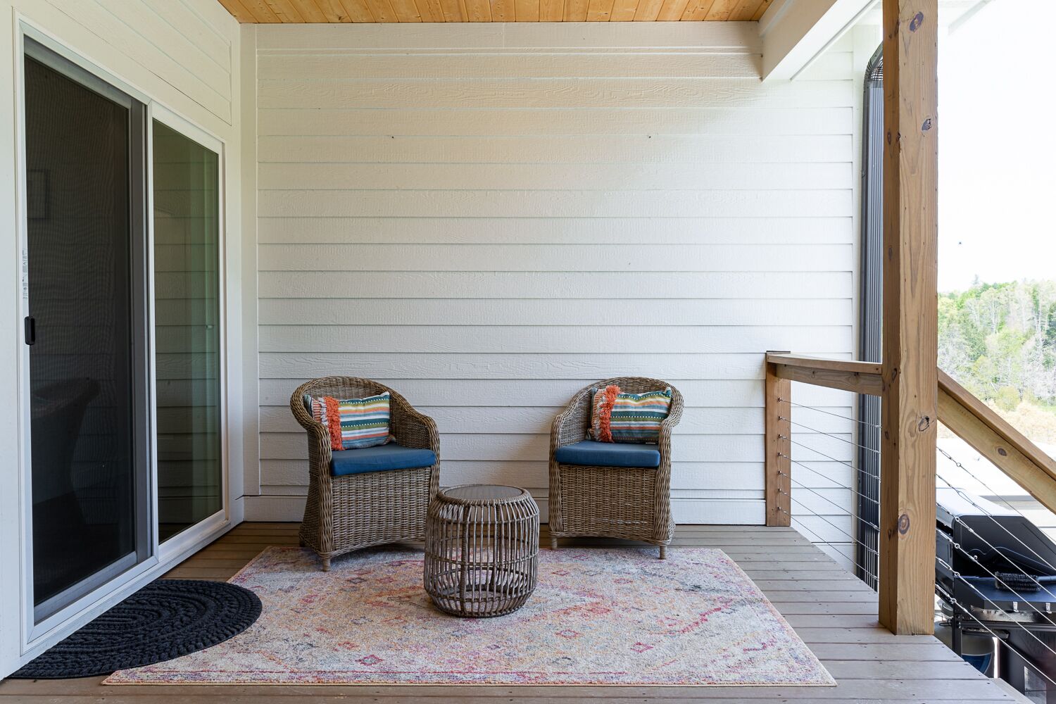 Une véranda avec deux fauteuils en osier, une petite table ronde et un tapis aux couleurs vives.