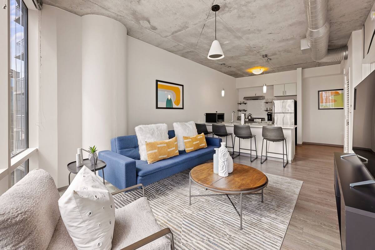 A modern living room with a blue sofa, a wooden coffee table, and a kitchen in the background.