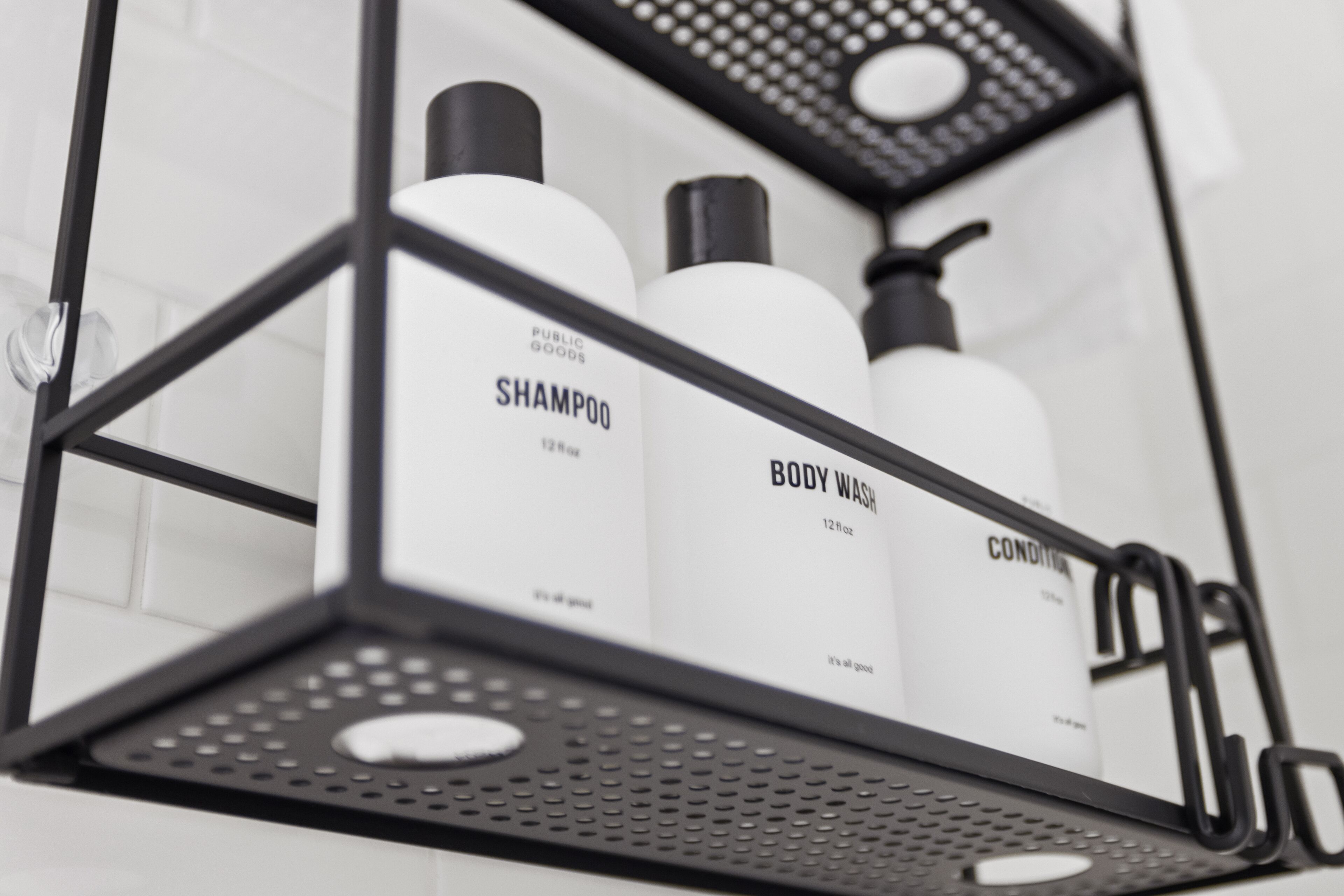 Estante metálico con tres botellas etiquetadas como 'Shampoo', 'Body Wash' y 'Conditioner'.