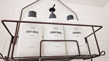 A metal rack with three white bottles labeled 'PUBLIC GOODS BODY WASH', 'PUBLIC GOODS CONDITIONER', and 'PUBLIC GOODS SHAMPOO', each 12 fl oz.