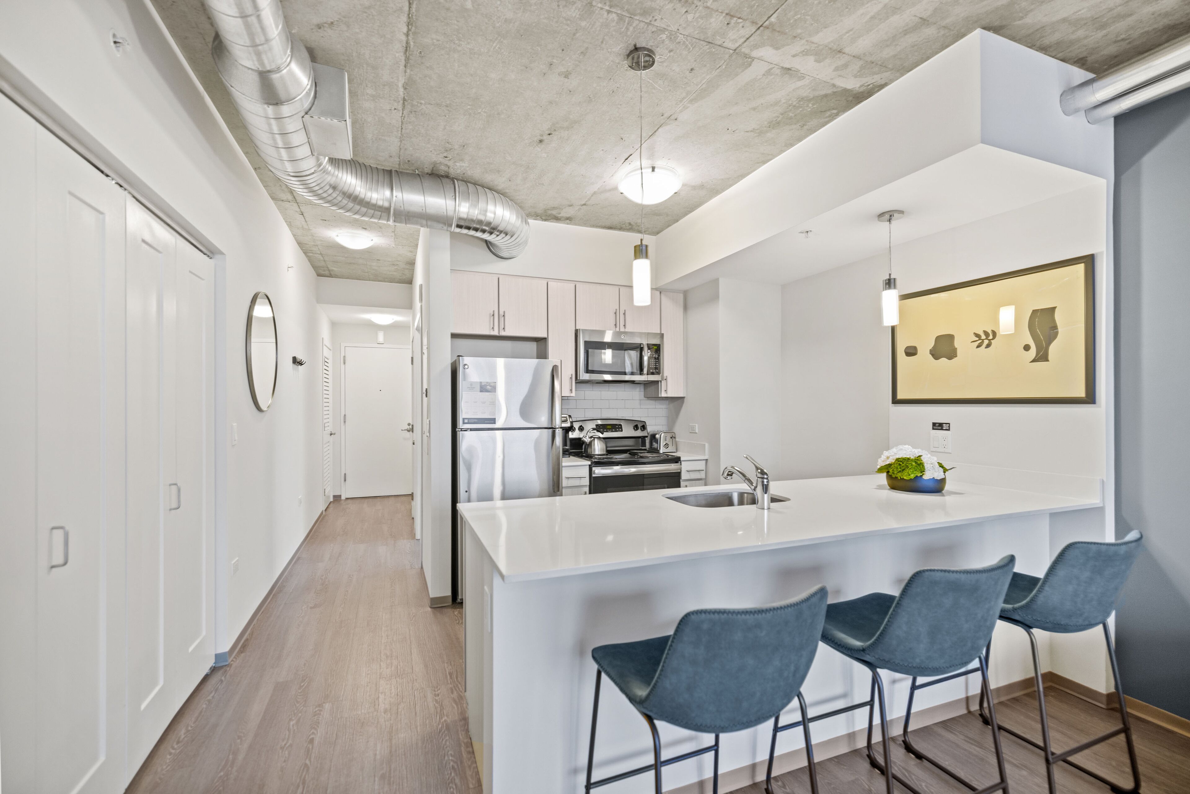 Una cocina moderna con muebles blancos, electrodomésticos de acero inoxidable y una isla central con taburetes de bar.