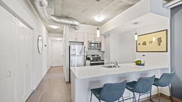 Una cocina moderna con muebles blancos, electrodomésticos de acero inoxidable y una isla central con taburetes de bar.