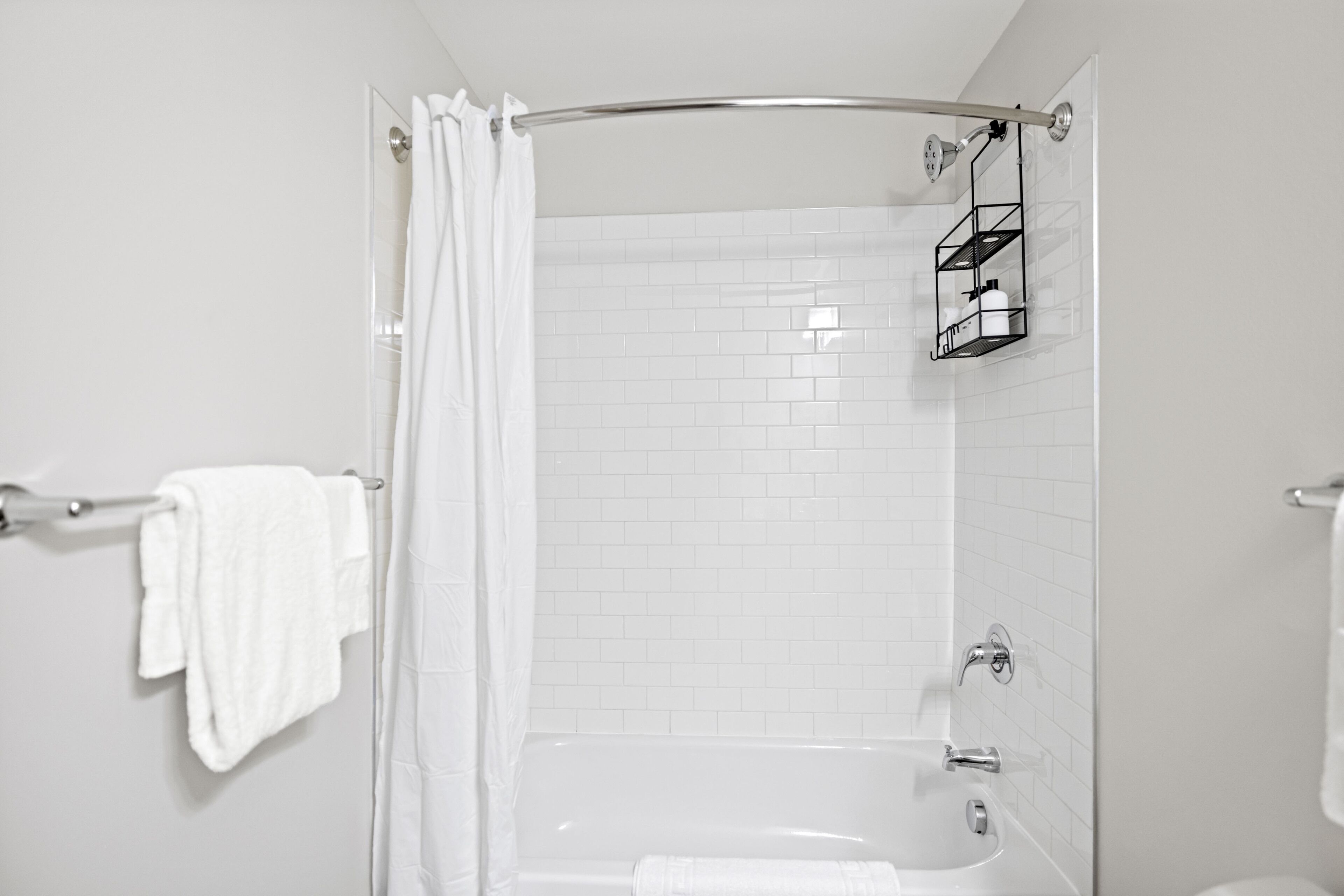 A modern bathroom with a glass shower enclosure, white tiled walls, and a built-in shelf with toiletries.
