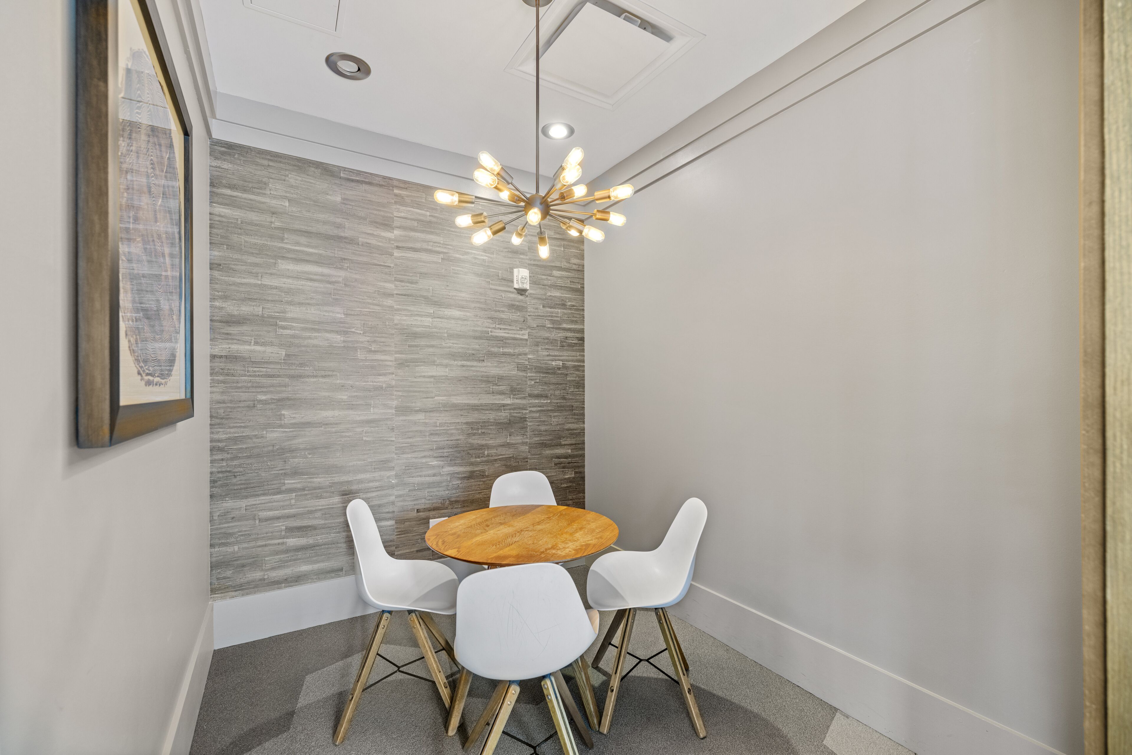 Een vergaderruimte met een ronde houten tafel, witte stoelen en een moderne kroonluchter.
